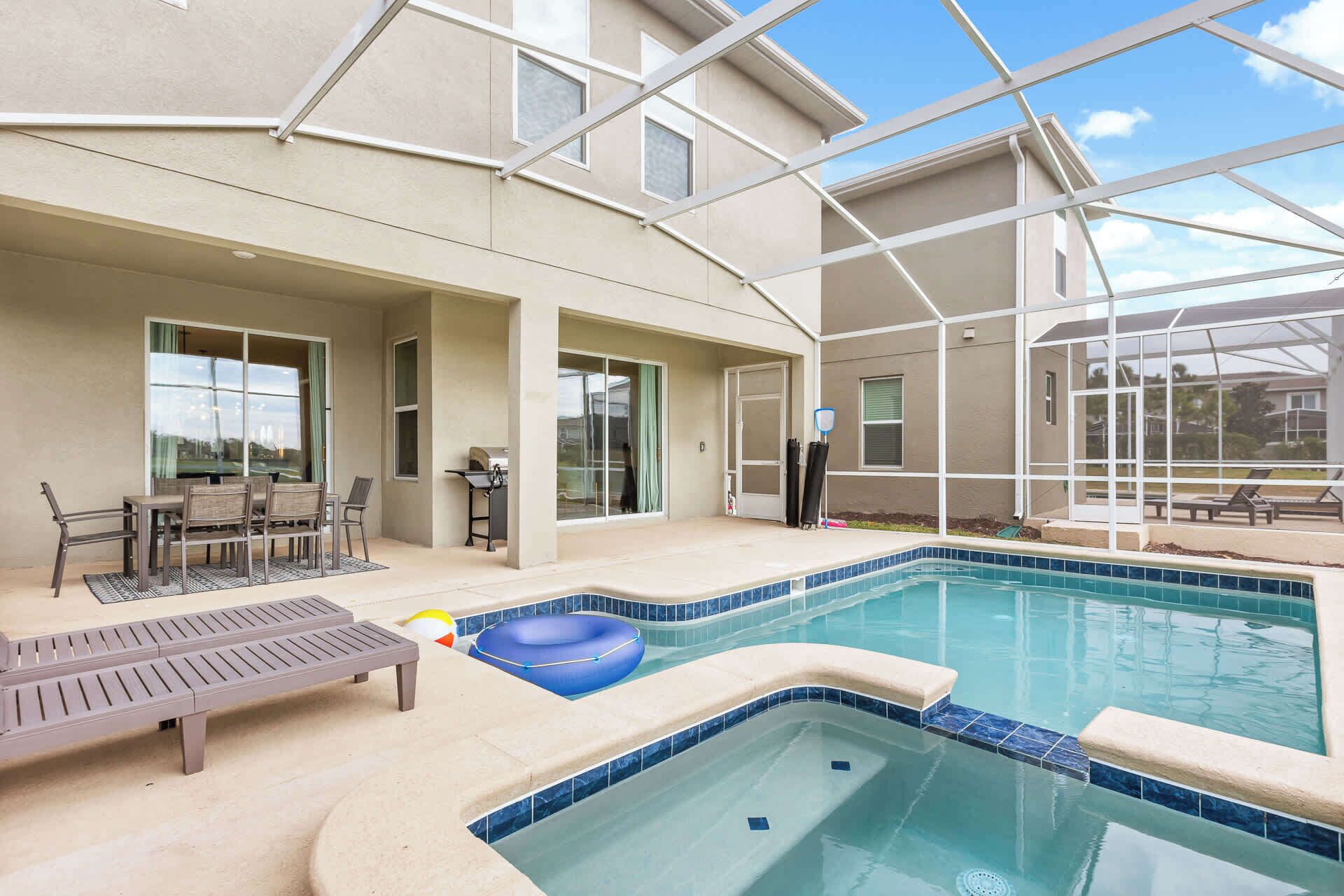 An indoor swimming pool with a sunroof, a lounge area with chairs, and a table.