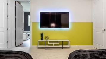 Un dormitorio moderno con un televisor montado en la pared, una mesita de noche con una planta y una puerta que da a otra habitación.