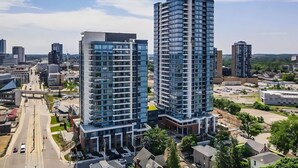 A high-rise building with a modern glass facade, surrounded by other buildings and a clear sky. - Stylish 1BR Condo w Balcony & Skyline Views (Kitchener)