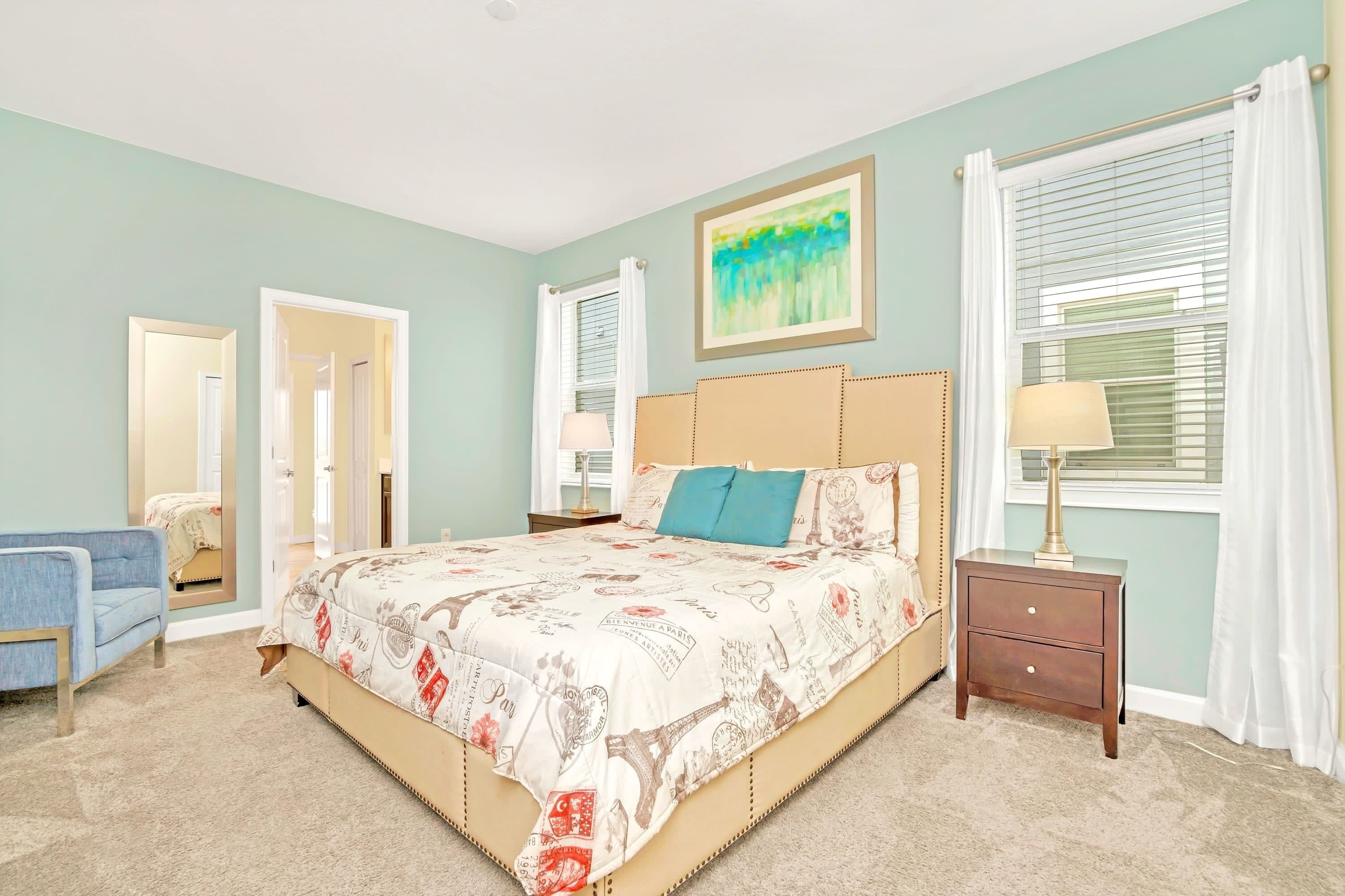A bedroom with a large bed, a nightstand, a chair, and a window with curtains.