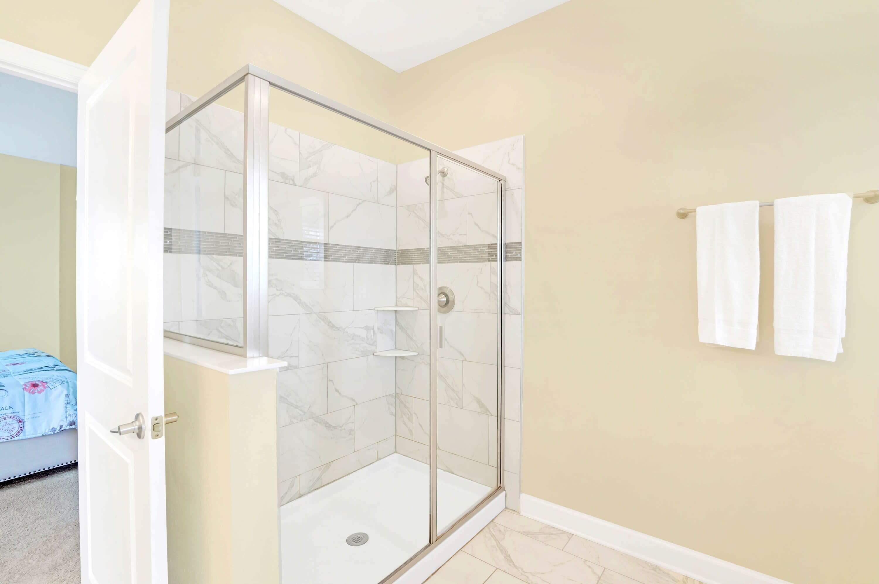 A modern bathroom with a glass-enclosed shower, beige walls, and a towel rack.