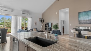 A modern kitchen with a large island, a built-in sink, and a dining area with bar stools. - Large 6BR Lakefront Home With Private Pool & Views (Lakeway)