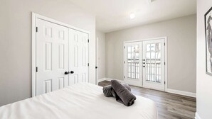 Ein Schlafzimmer mit einem Bett, zwei weißen Türen und Blick durch eine Glastür.