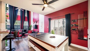 Ein Zimmer mit Tischtennisplatte, Deckenventilator, Billardständer und einer roten Wand.