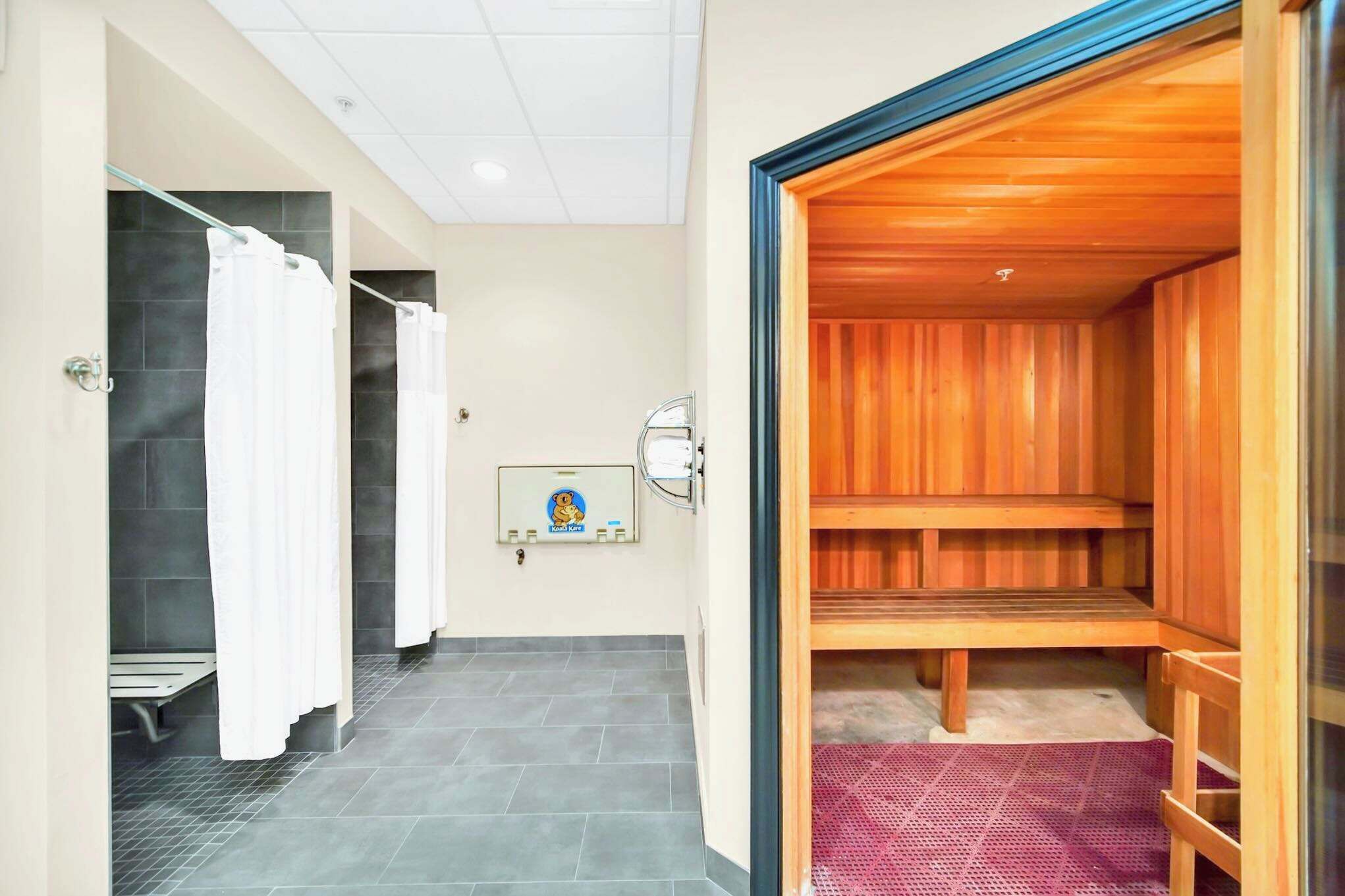 A modern bathroom with a shower area, a wooden sauna, and a bench.