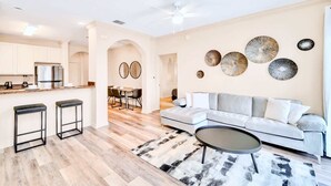 A modern living room with a sofa, coffee table, and a dining area with chairs and a table. - Family Fun Condo Pool and Sauna Near Disney (Winter Garden)