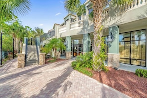 A multi-story hotel with a brick pathway, palm trees, and a gated entrance. - Upstay - LRG Condo w Outdoor Pool, Sauna (Winter Garden)