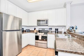 Uma cozinha moderna com armários brancos, eletrodomésticos de aço inoxidável, bancadas de granito e piso revestido.