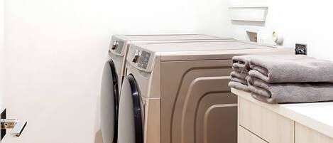 A laundry room with two front-loading washing machines, a wooden floor, and a white wall.