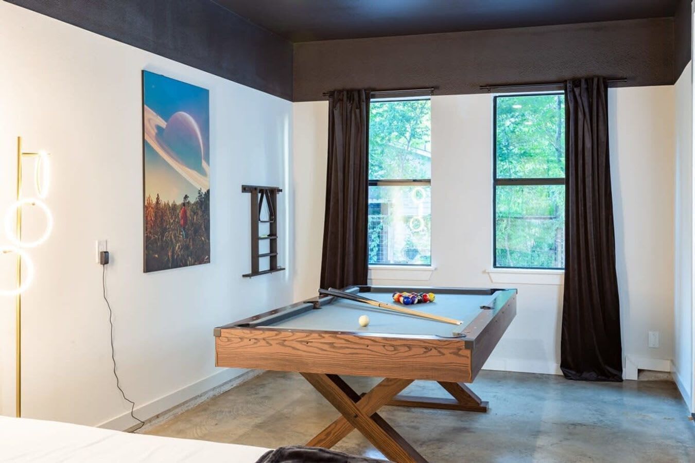 A pool table in a room with large windows, a ladder, and a painting on the wall.