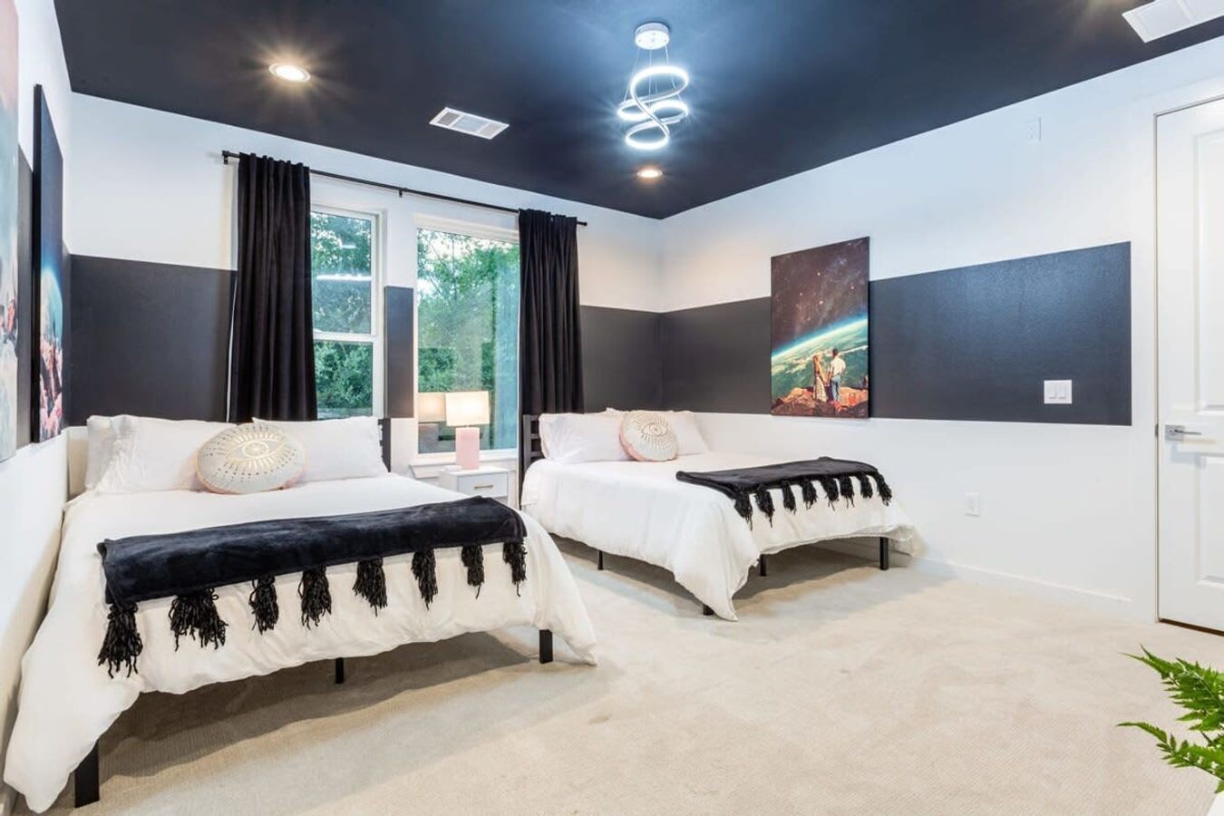 A modern bedroom with two beds, a large window, and a painting on the wall.