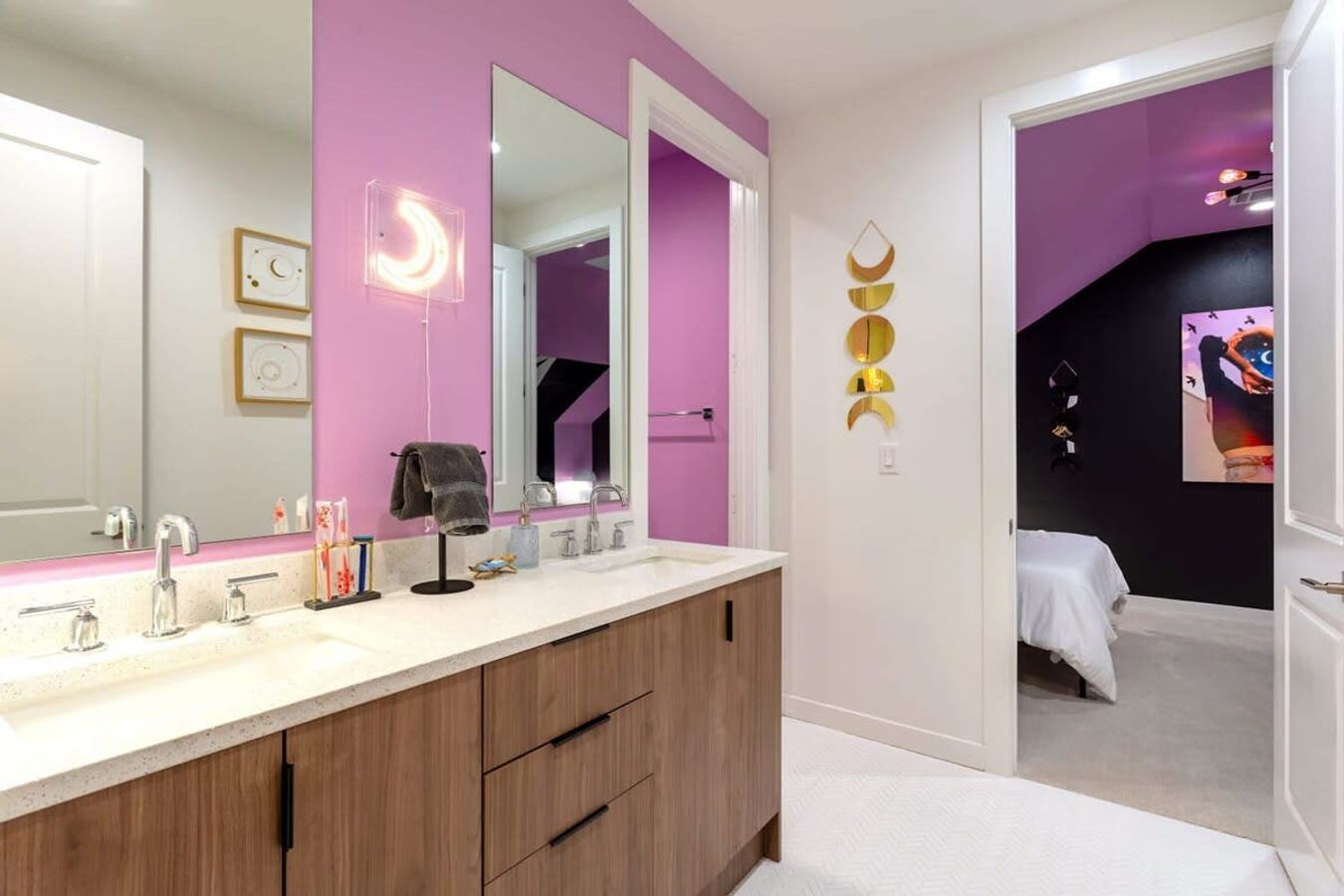 A modern bathroom with a pink wall, a large mirror, and a vanity with a wooden cabinet.
