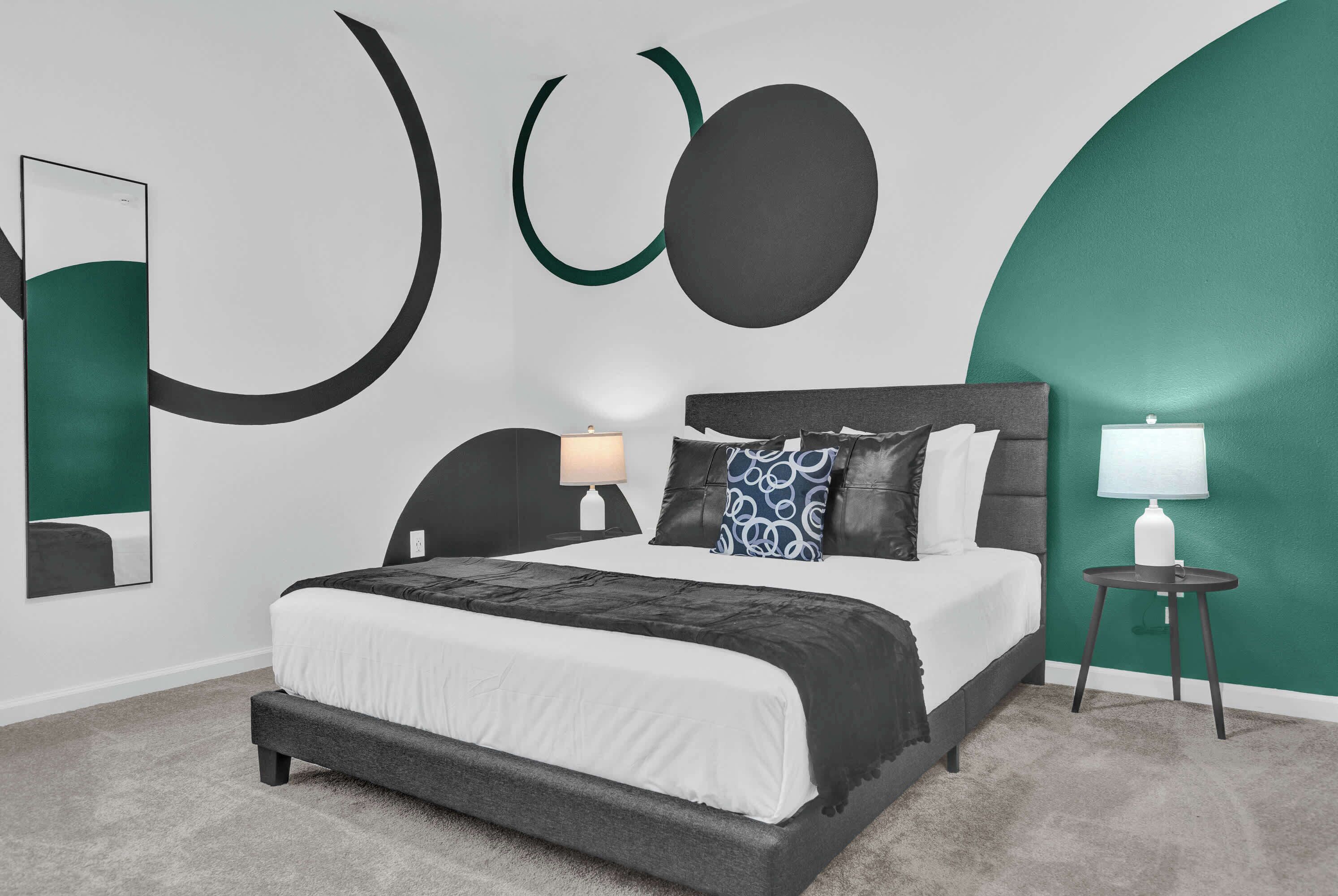 Ein modernes Schlafzimmer mit einem großen Bett, einem Nachttisch mit Lampe und abstrakter Wandkunst.
