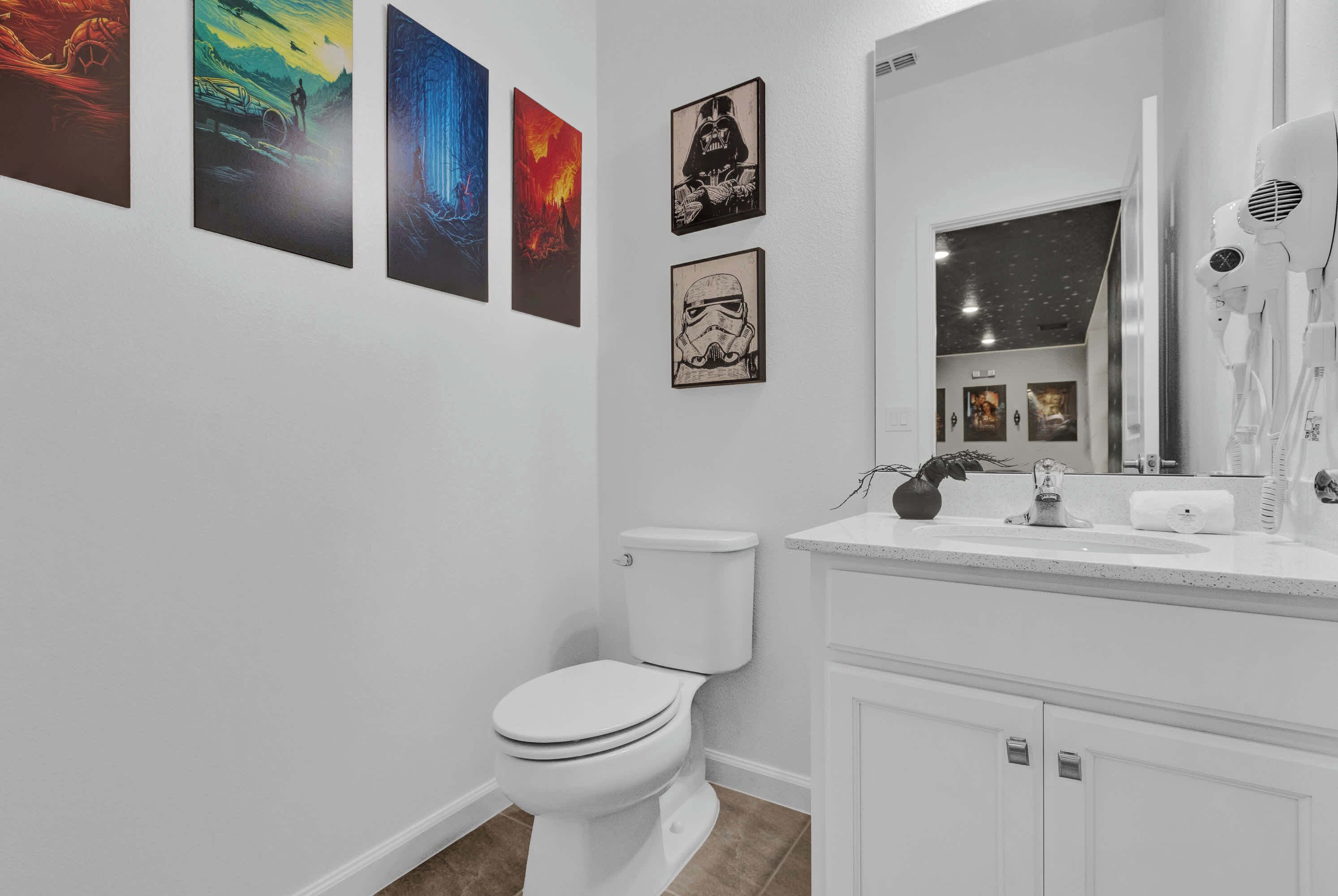 A bathroom with a white toilet, a sink with a mirror, and four framed pictures on the wall.