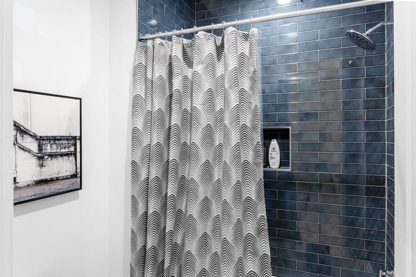 Une salle de bain avec un rideau de douche orné d’un motif ondulé noir et blanc, un mur carrelé et un tableau encadré accroché au mur.