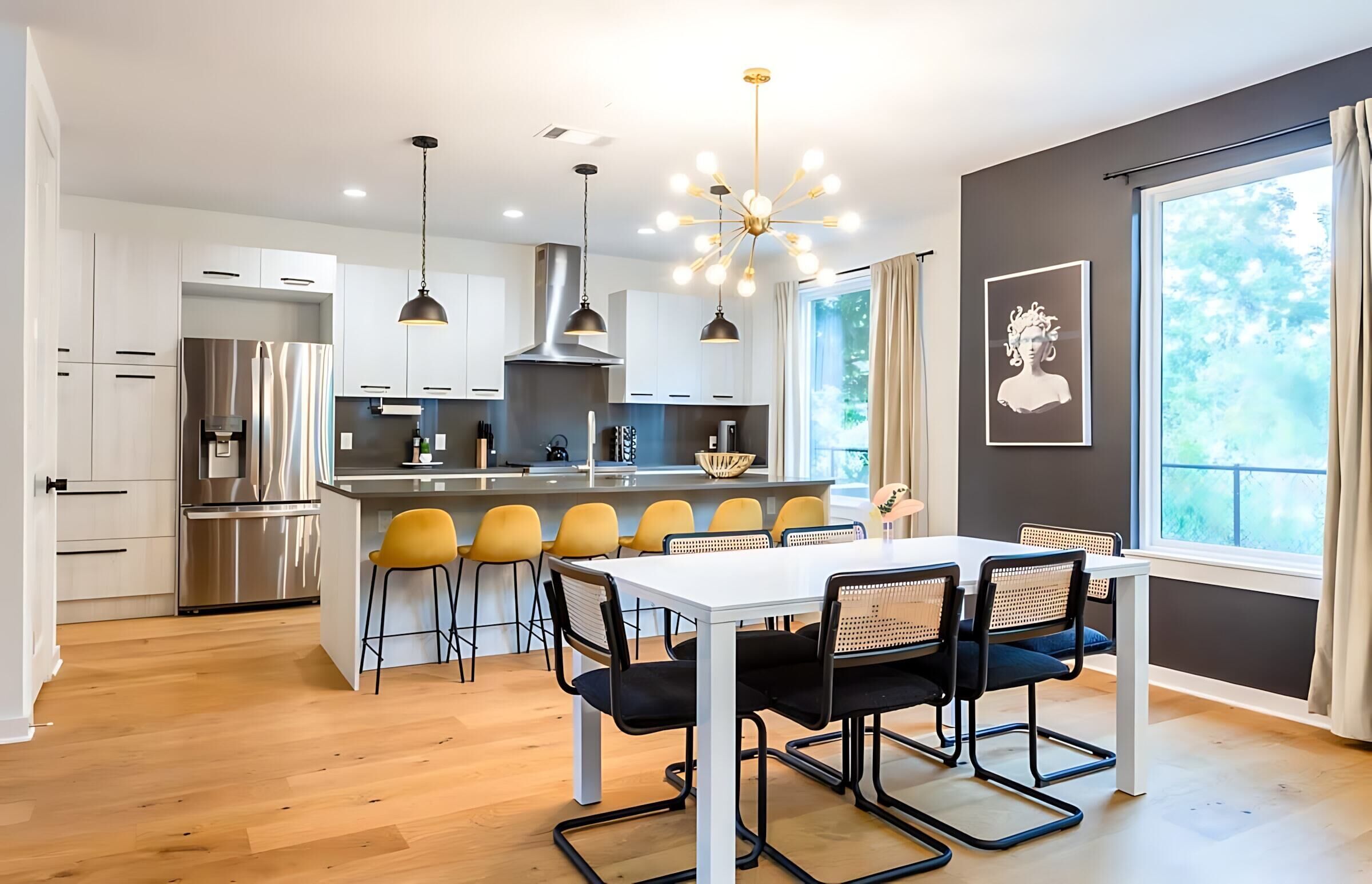 A modern kitchen with a central island, stainless steel appliances, and a dining area with a white table and yellow chairs.
