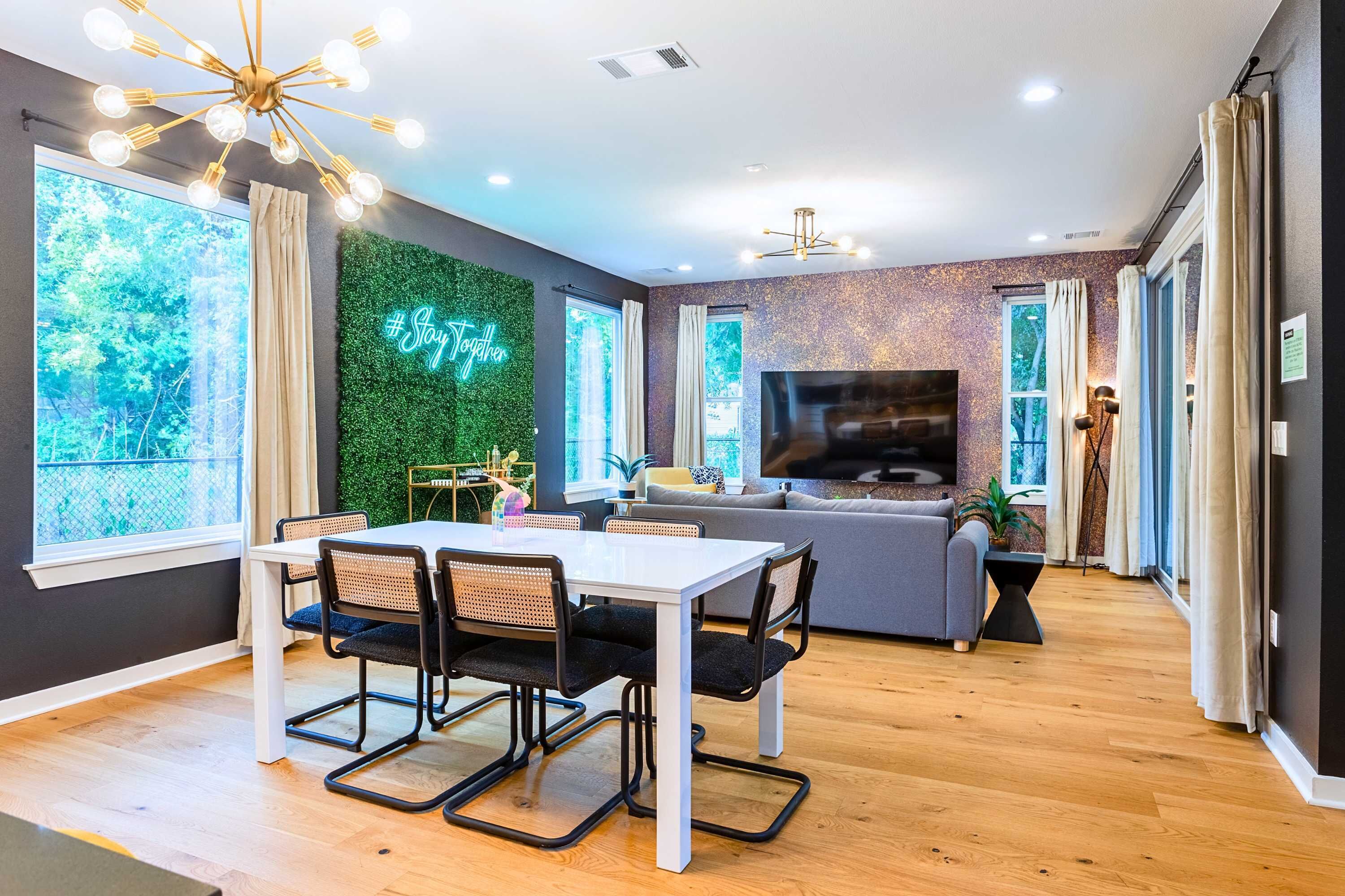 Una sala de estar moderna con comedor, ventanas amplias, una pared verde y televisor.