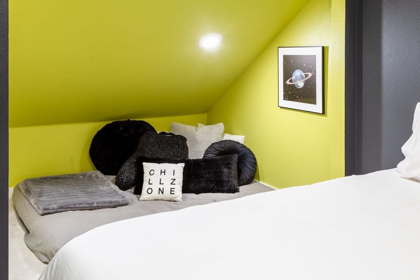 A bedroom with a sloped ceiling, a bed with white bedding, and a pillow with "CHILL ONE" text.