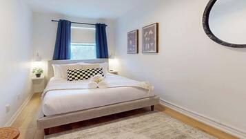 A neatly arranged bedroom with a bed, bedside tables, a potted plant, and artwork on the wall.