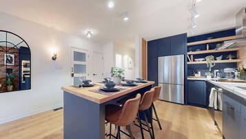 A modern kitchen with a central island, bar stools, a stainless steel refrigerator, and a built-in oven.