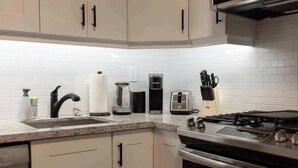 Una cocina con armarios blancos, estufa a gas, cafetera y tostadora.