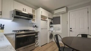 Cocina compacta con estufa, horno, microondas y lavadora integrada. Hay una mesa de comedor con sillas y una puerta blanca.