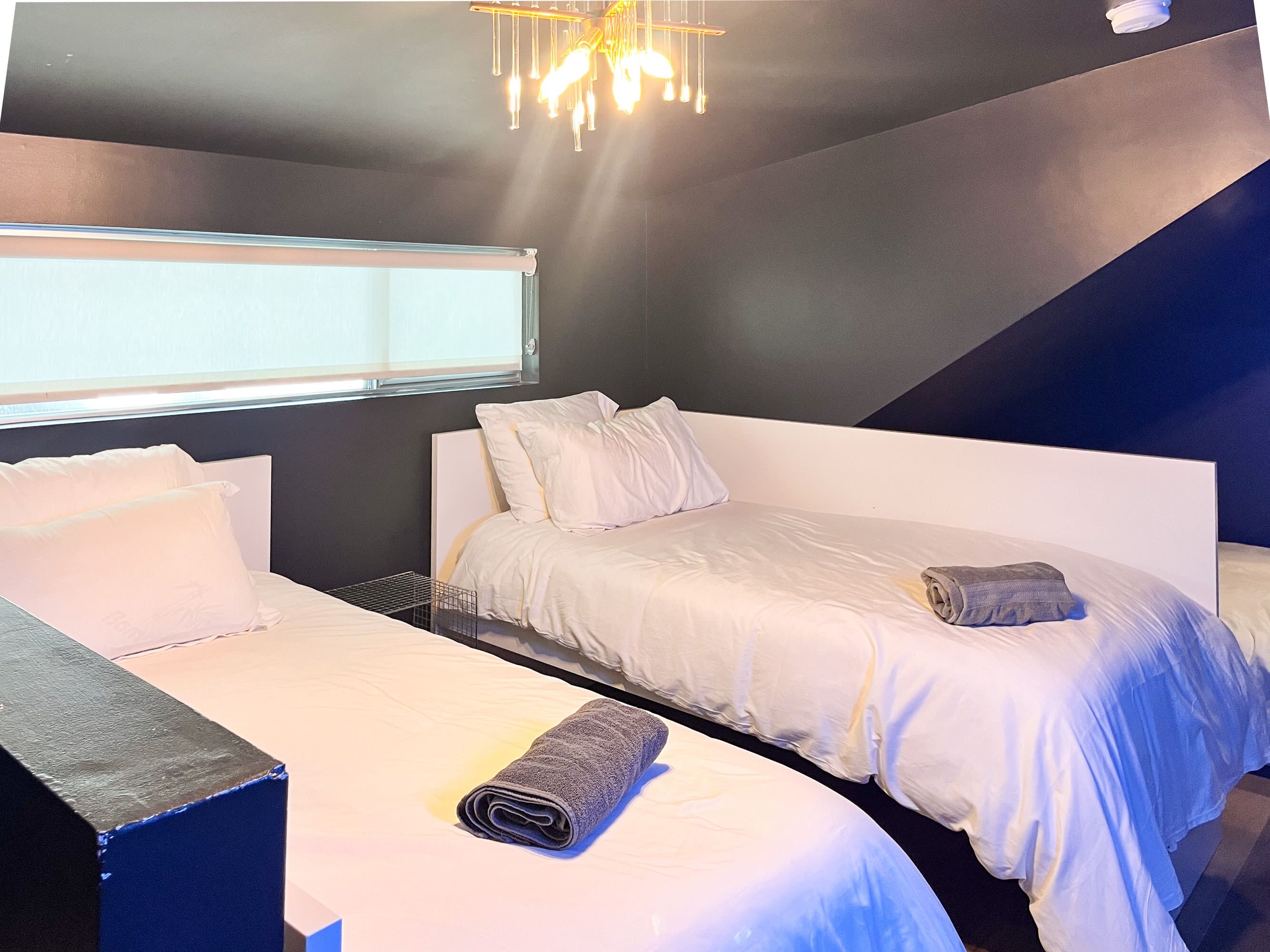 A hotel room with two beds, a window, and a modern chandelier.