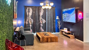 Ein modernes Wohnzimmer mit blauer Akzentwand, einem schwarzen Sofa, einem Holztisch und einem an der Wand montierten Fernseher.