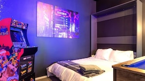 Ein Schlafzimmer mit einem Bett, einem Nachttisch, einem Wandfernseher und einer Spielkonsole.
