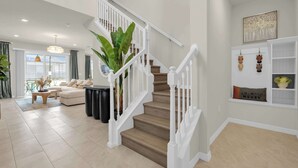 A staircase with white railings, a living room with a sofa and coffee table, and a window with curtains. - Upstay Disney 5BR Movie Mansionwindsor Cay Resort (Clermont)