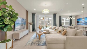 A modern living room with a sectional sofa, a flat-screen TV, a dining area, and a large plant. - Upstay Disney 5BR Movie Mansionwindsor Cay Resort (Clermont)