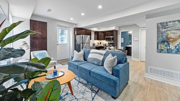 A modern living room with a blue sofa, a coffee table, and a kitchen in the background. - Stylish Modern Family Suite With Patio (Toronto)