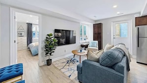 A modern living room with a sofa, a coffee table, a TV, and a potted plant. - Stylish Modern Family Suite With Patio (Toronto)