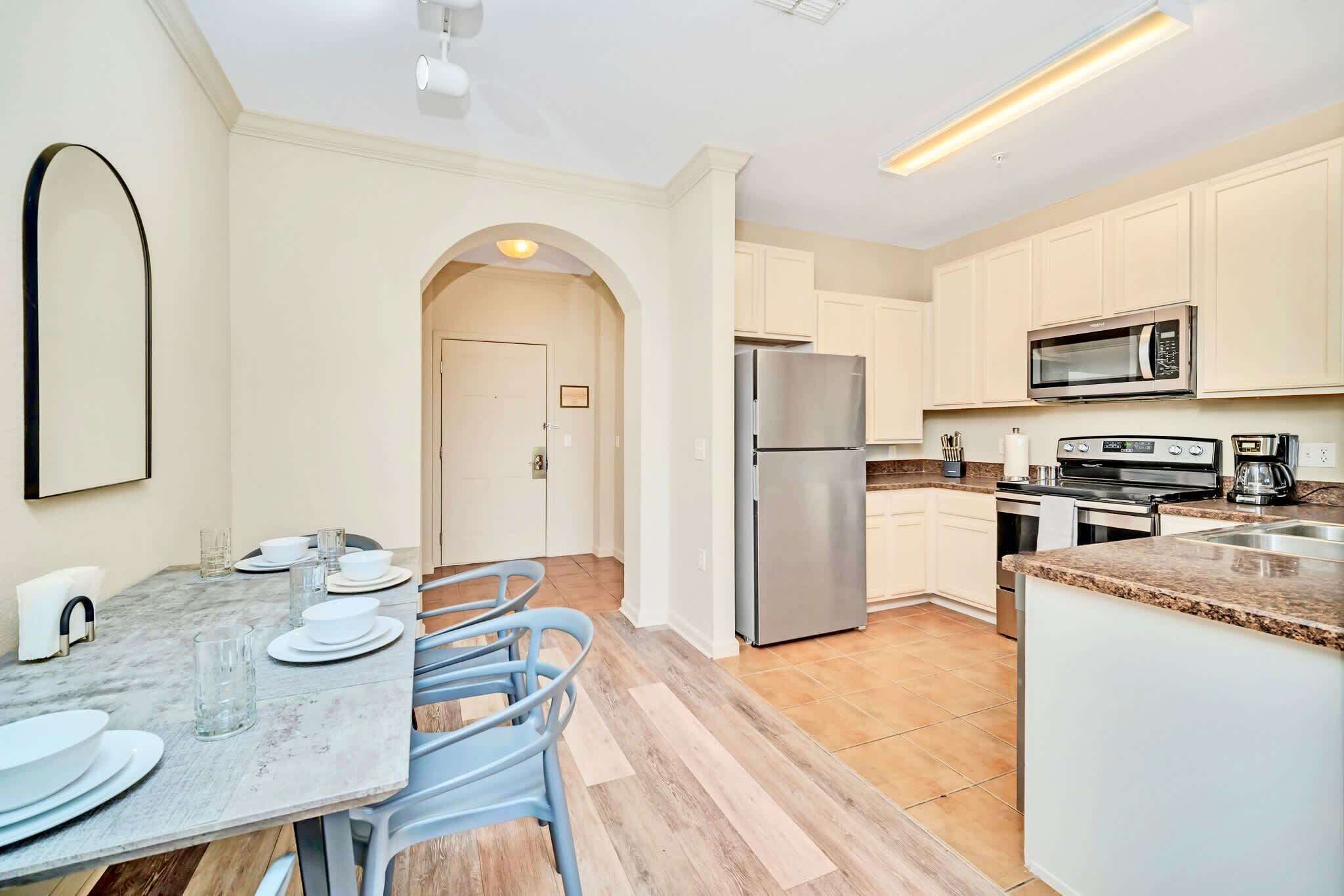 A modern kitchen with white cabinets, stainless steel appliances, and a dining area with a marble table and blue chairs.