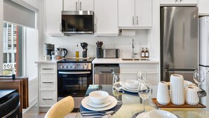 A modern kitchen with white cabinets, stainless steel appliances, and a dining area set with white plates and wine glasses. - The Mccaul Cozy DT Suite Near Fifa 2026 (Toronto)