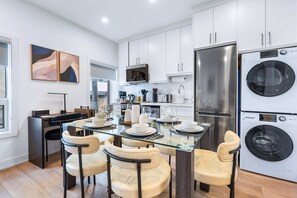 A modern kitchen with white cabinets, stainless steel appliances, and a dining area with glass tables and chairs. - The Mccaul Cozy DT Suite Near Fifa 2026 (Toronto)