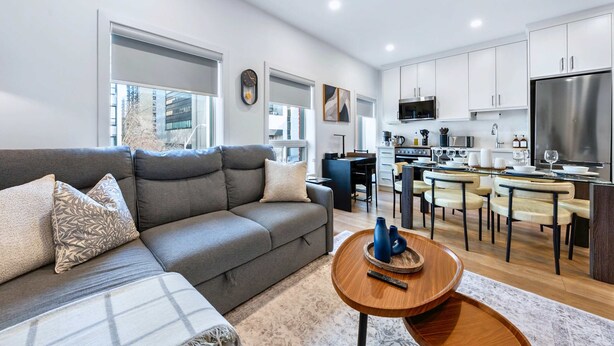 A modern living room with a sofa, a coffee table, and a kitchen area with cabinets and appliances. - The Mccaul Cozy DT Suite Near Fifa 2026 (Toronto)