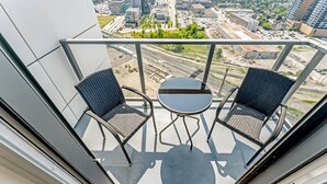 A balcony with two wicker chairs and a small table, overlooking a cityscape with buildings and roads. - Newly Built Modern Condo With Stunning City Views (Kitchener)