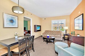 A living room with a sofa, a dining table with chairs, a TV, and a lamp. - Near Disney King Bed Condo Unit - Pool & Hot Tub! (Orlando)