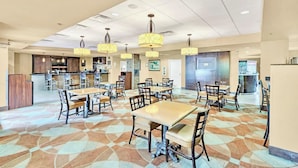 A spacious dining area with multiple tables and chairs, a kitchen in the background, and pendant lighting. - Near Disney King Bed Condo Unit - Pool & Hot Tub! (Orlando)
