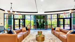 A spacious lobby with leather sofas, a central coffee table, and large windows offering a view of greenery outside. - Upstay: Pet-friendly Family Condo w Poolsleeps 8 (Winter Garden)