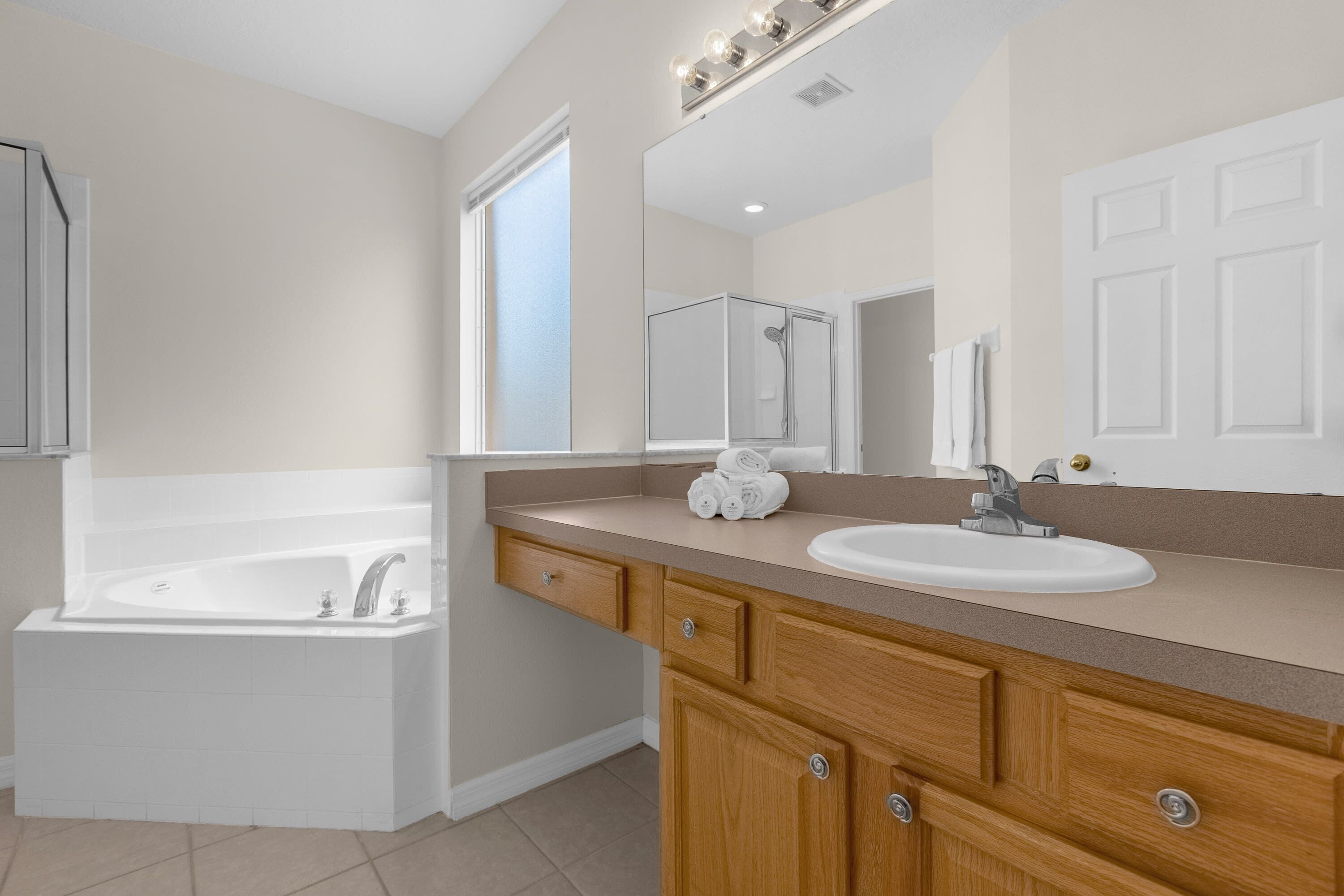 A bathroom with a bathtub, a sink, a vanity with drawers, and a mirror.