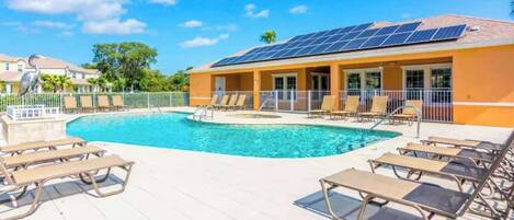 A swimming pool with lounge chairs, a building with solar panels, and a fenced area.