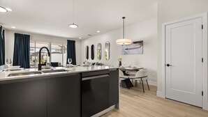 A modern kitchen with a central island, a dining area with a table and chairs, and a white door. - Contemporary 4BR Townhome With Pool & Themed Rooms (Clermont)