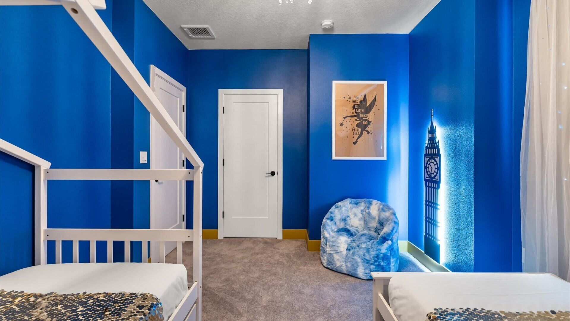 Een kamer met blauwe wanden, een witte deur, stapelbedden, een blauwe kruikenzak en een lijst met een motiverende quote.
