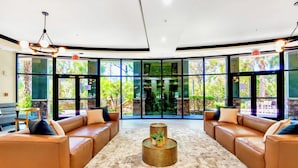 A spacious lobby with leather sofas, a central coffee table, and large windows offering a view of greenery outside. - Upstay 3BR Suite w Pool, Sauna & Gamesnear Disney (Winter Garden)