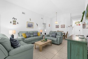 Un salon moderne avec deux canapés verts, une table basse en bois et un coin repas comprenant une table et des chaises.