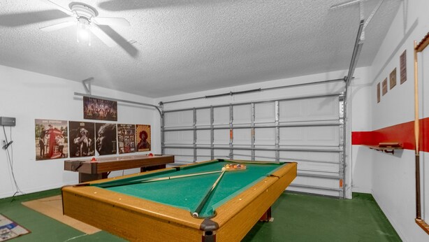 Une table de billard dans une pièce dotée d’une porte de garage, d’un revêtement de sol vert et d’un ventilateur de plafond.