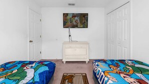 Une chambre avec deux lits, une commode, un ventilateur de plafond et un téléviseur fixé au mur.