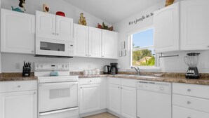 Une cuisine moderne avec des meubles blancs, un four encastré, un four à micro-ondes, une machine à café et un mixeur.